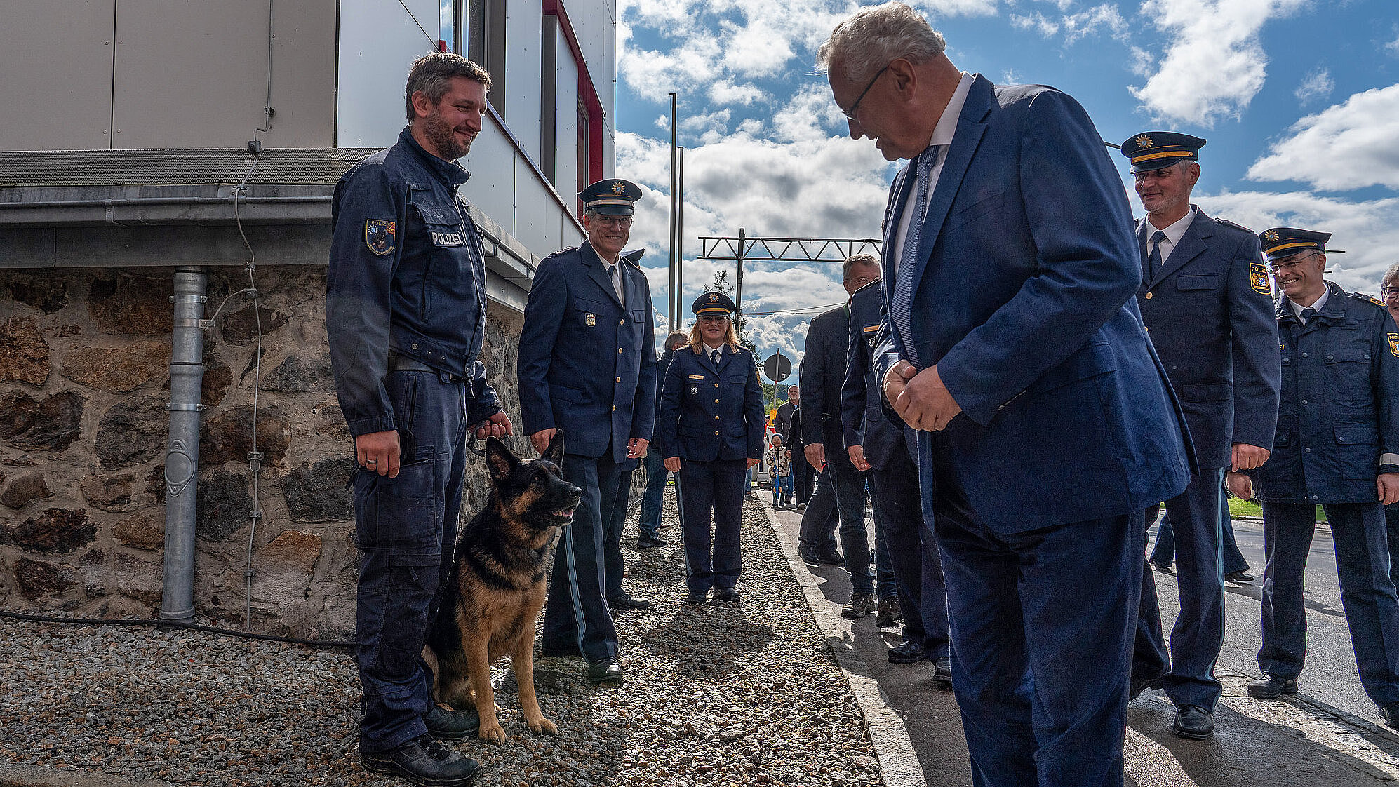 Innenminister Joachim Herrmann blickt zu einem Schäferhund neben Polizist, im Hintergrund weitere Polizisten