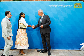 Zwei Gäste vor der blauen Pressewand des StMI im Gespräch mit Innenminister Joachim Herrmann.