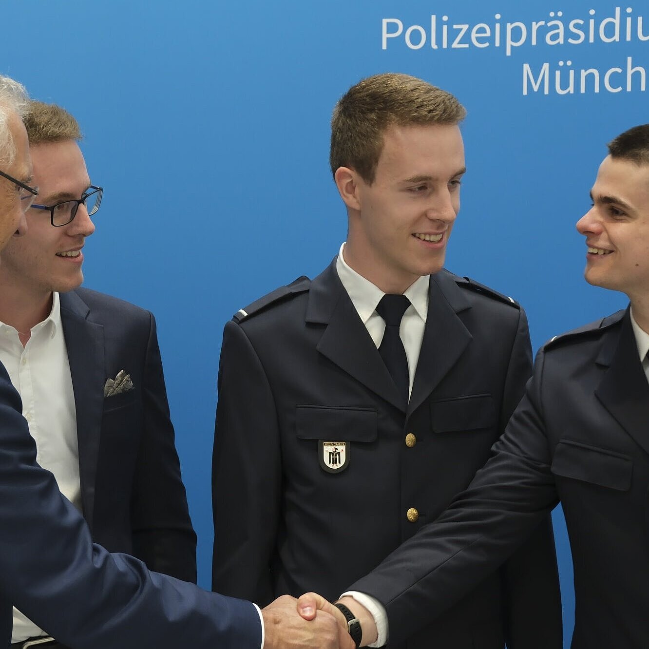Auf dem Bild ist Innenminister Joachim Herrmann mit jungen Polizisten zu sehen, einem davon schüttelt er lächelnd die Hand.