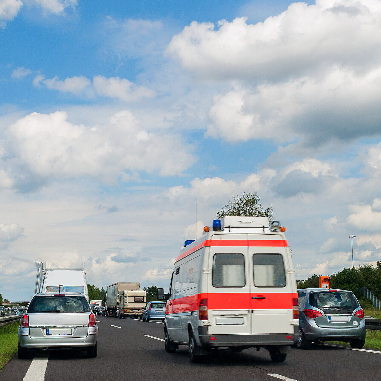 Auf dem Bild ist ein Krankenwagen zu sehen, wie dieser durch eine Rettungsgasse auf der Autobahn fährt. Links und rechts von ihm sind stehende Autos zu sehen.