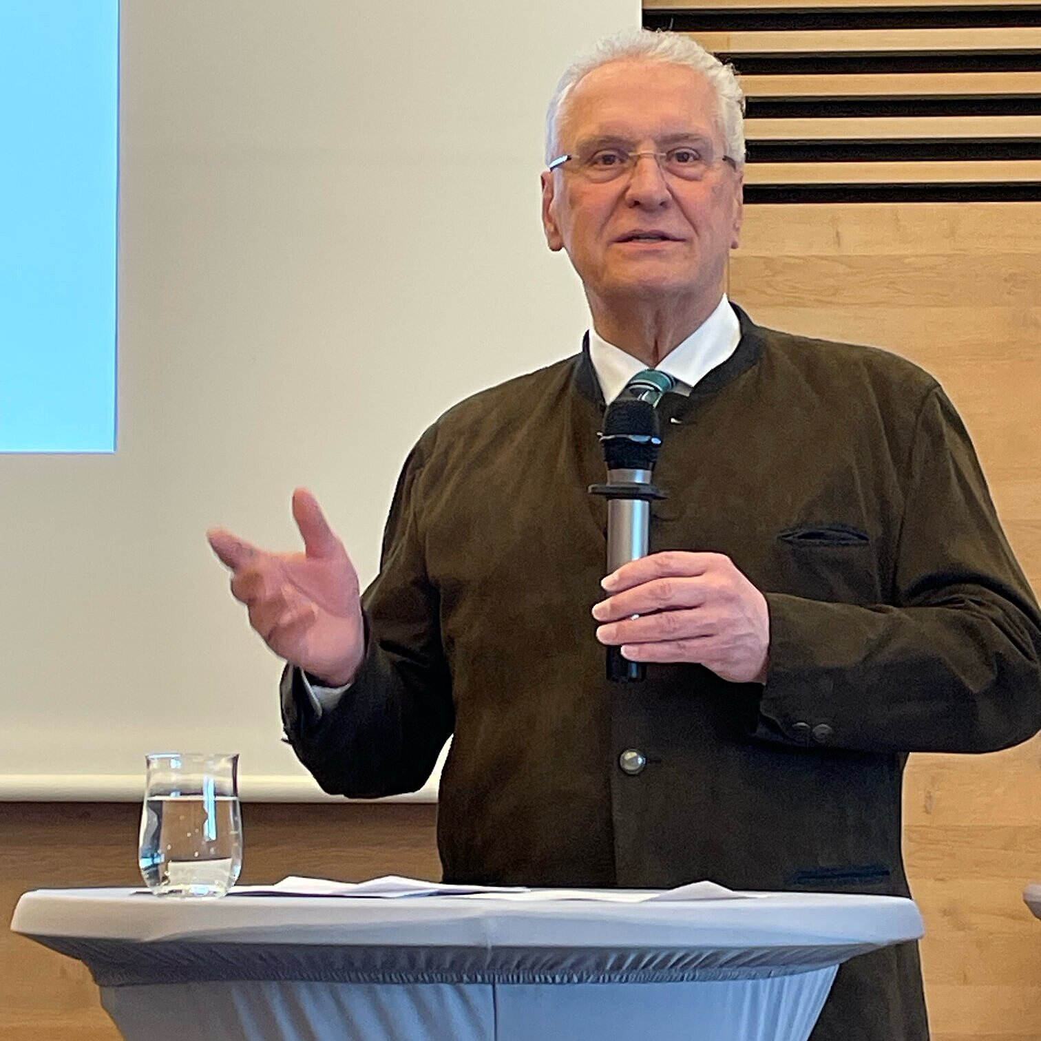 Es ist Innenminister Joachim Herrmann während seiner Rede an einem Stehtisch zu sehen, in der Hand hält er ein Mikrofon