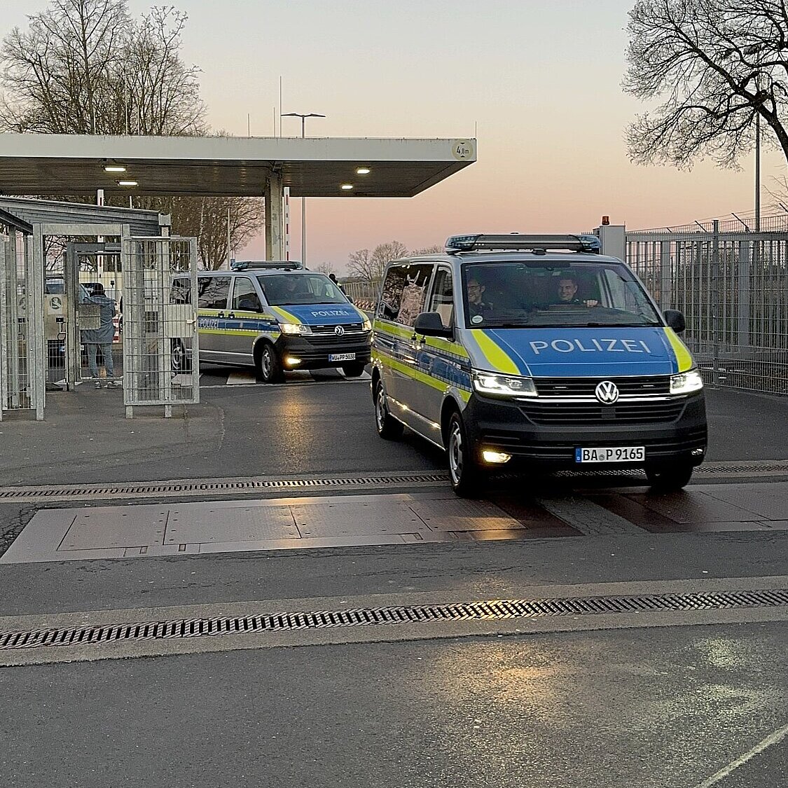 Zwei Polizeifahrzeuge fahren aus einem Gelände heraus auf die Straße