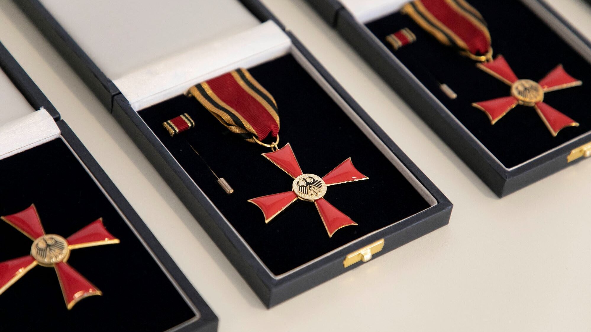 Auf dem Bild sind drei Bundesverdienstkreuze am Bande nebeneinander aufgereiht in ihrer jeweiligen Aufbewahrungsschatulle zu sehen.