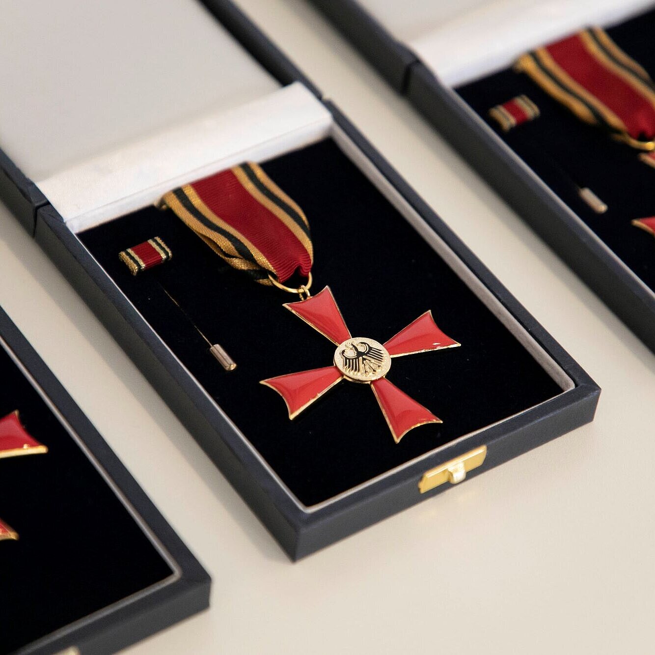 Auf dem Bild sind drei Bundesverdienstkreuze am Bande nebeneinander aufgereiht in ihrer jeweiligen Aufbewahrungsschatulle zu sehen.