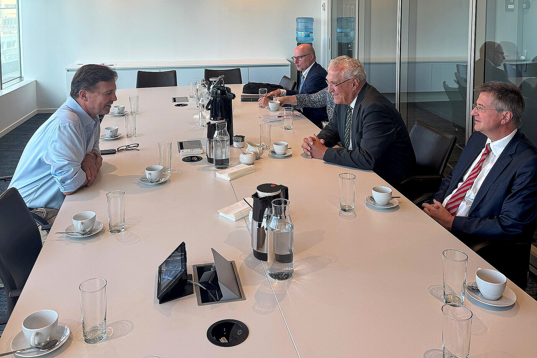 Innenminister Joachim Herrmann links im Bild, Steffen Seibert (gegenüber rechts im Bild)  u.a. sitzen um einen Tisch und interagieren miteinander.