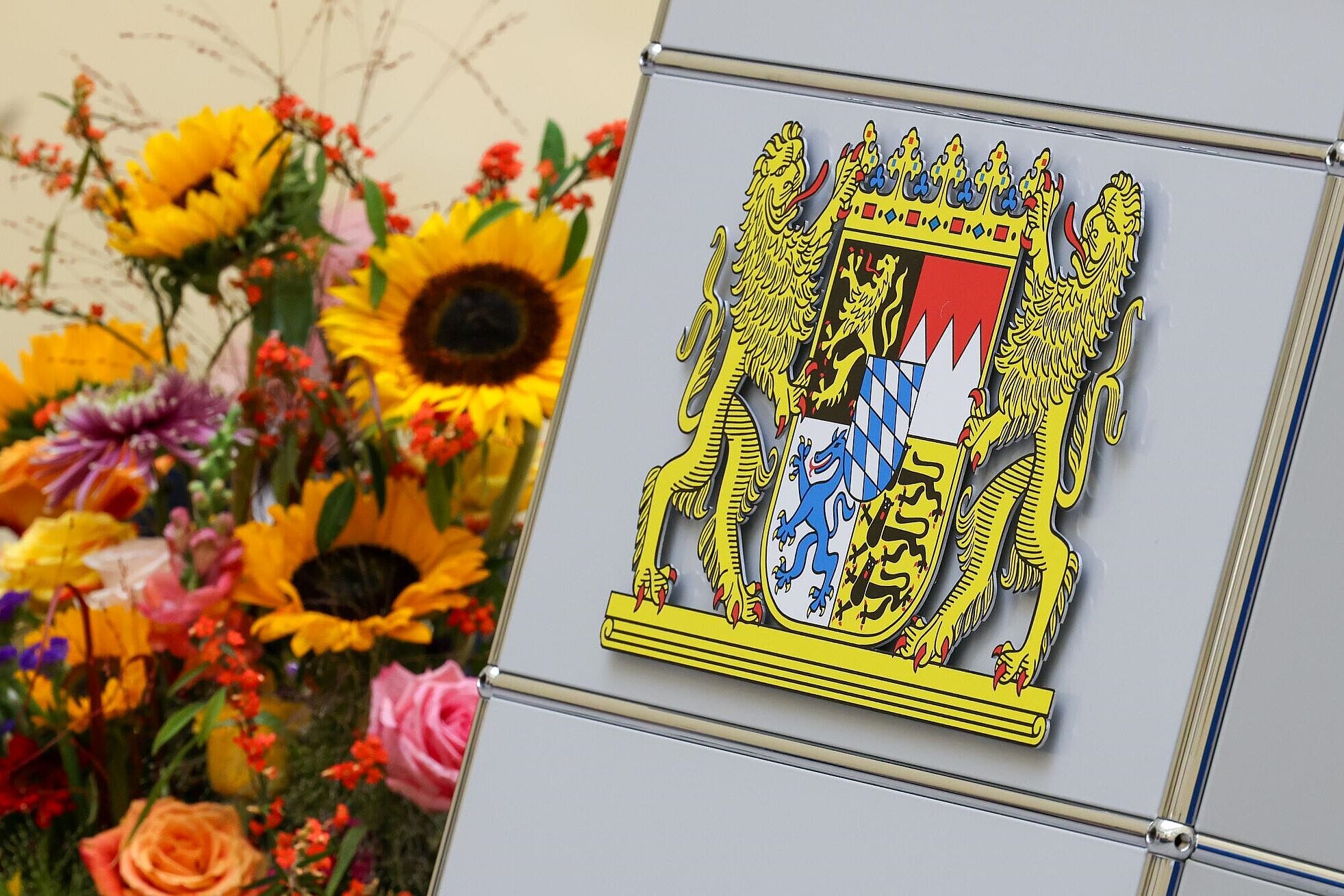Bayerisches Staatswappen aus Metall neben Blumen