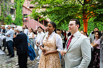 Zahlreiche Gäste im Innenhof der Kaiserburg Nürnberg beim Neubürgerempfang. Die Gäste blicken zur Bühne. Im Hintergrund leuchten warme Lichter und eine große Blumendekoration mit Sonnenblumen sorgt für festliches Ambiente.