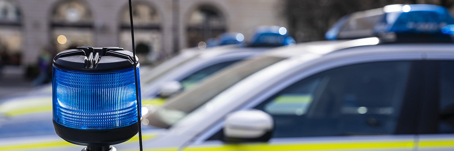 Im Vordergrund eine blaue Polizeileuchte und im Hintergrund mehre Polizeiautos