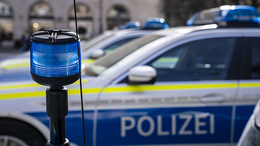 Im Vordergrund eine blaue Polizeileuchte und im Hintergrund mehre Polizeiautos
