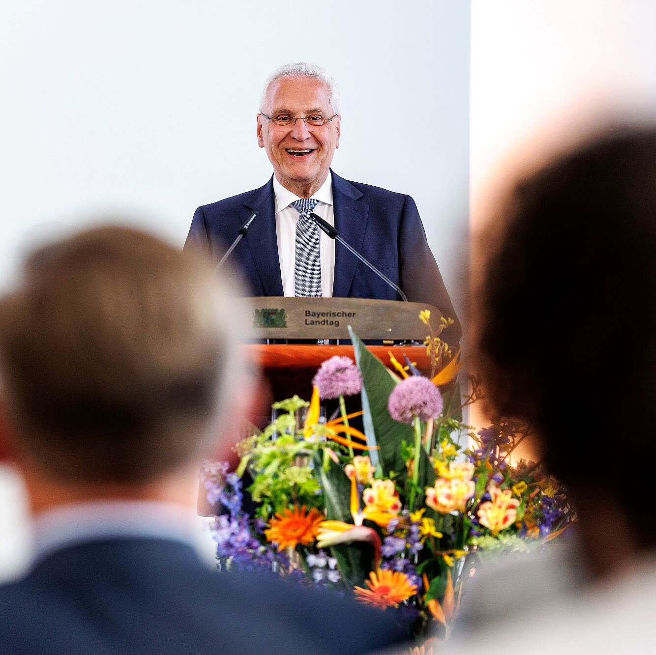 Innenminister Joachim Herrmann während seiner Rede am Rednerpult, vor ihm ein Blumendekor. Im Publikum sieht man Köpfe von hinten, die dem Minister zuhören.