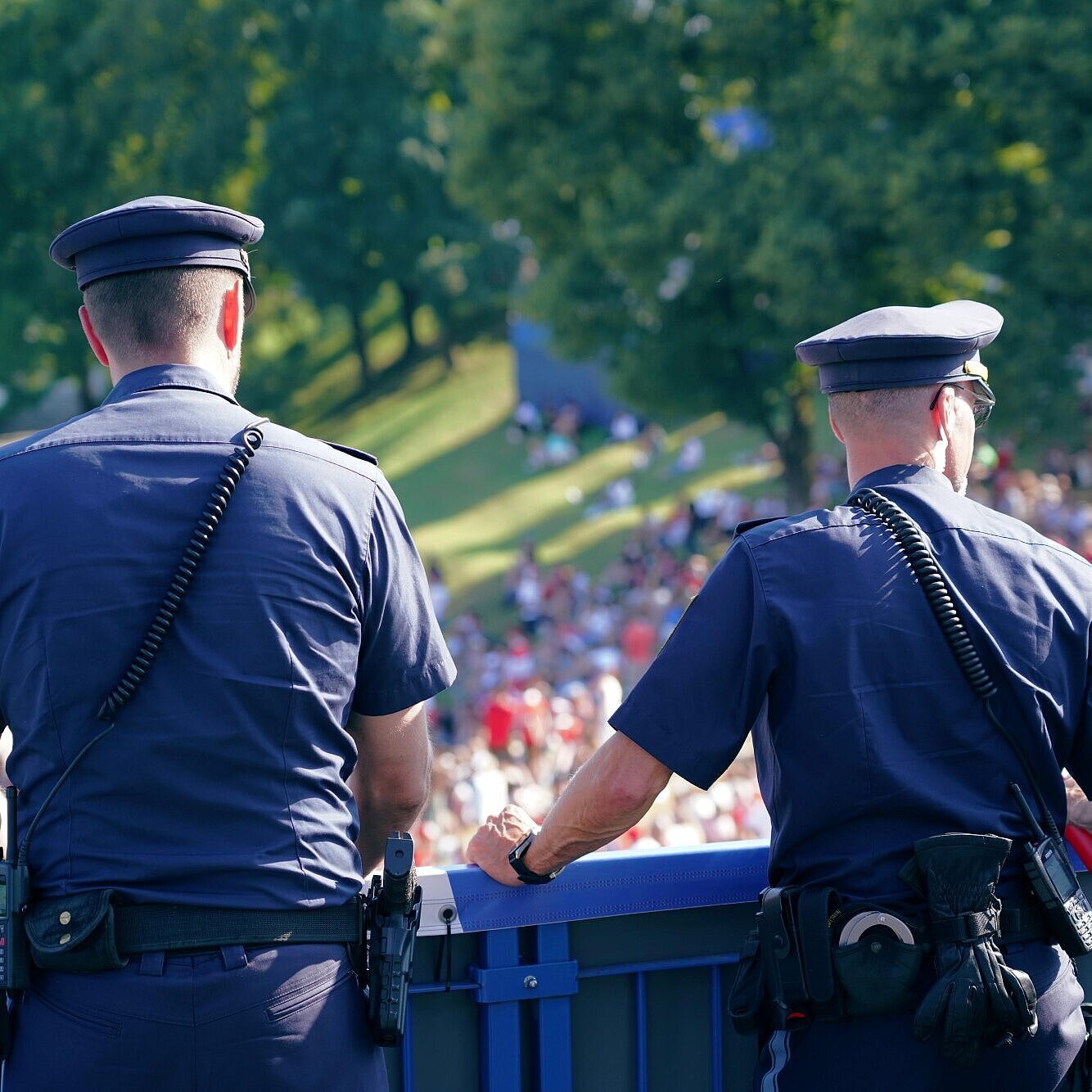 Auf dem Bild sind zwei Polizisten auf einer Brücke zu sehen, wie diese die Besucherströme bei einer Veranstaltung beobachten