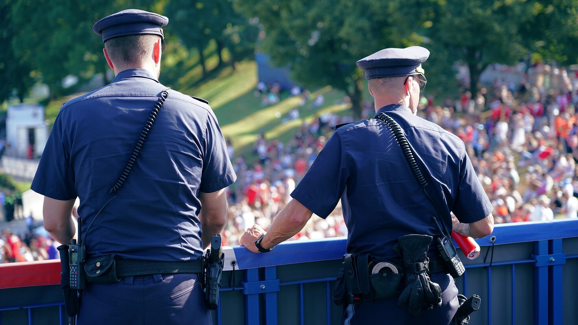 Auf dem Bild sind zwei Polizisten auf einer Brücke zu sehen, wie diese die Besucherströme bei einer Veranstaltung beobachten