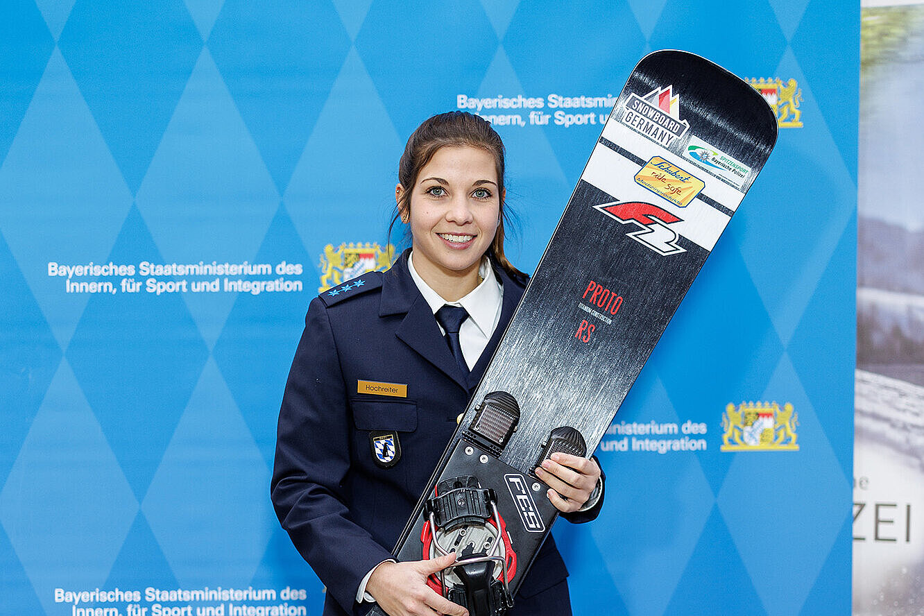 Melanie Hochreiter mit Snowboard in der Hand vor einer blauen Pressewand
