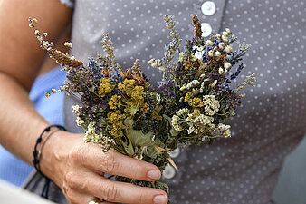 Auf dem Bild ist eine Dame im traditionellen Dirndl-Gewand zusehen, vor ihr ein gebundener Kräuterbusch, der geweiht wurde