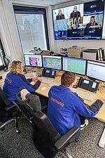 Mann und Frau vor Bildschirmen sitzend in einer Leitstelle Warnung