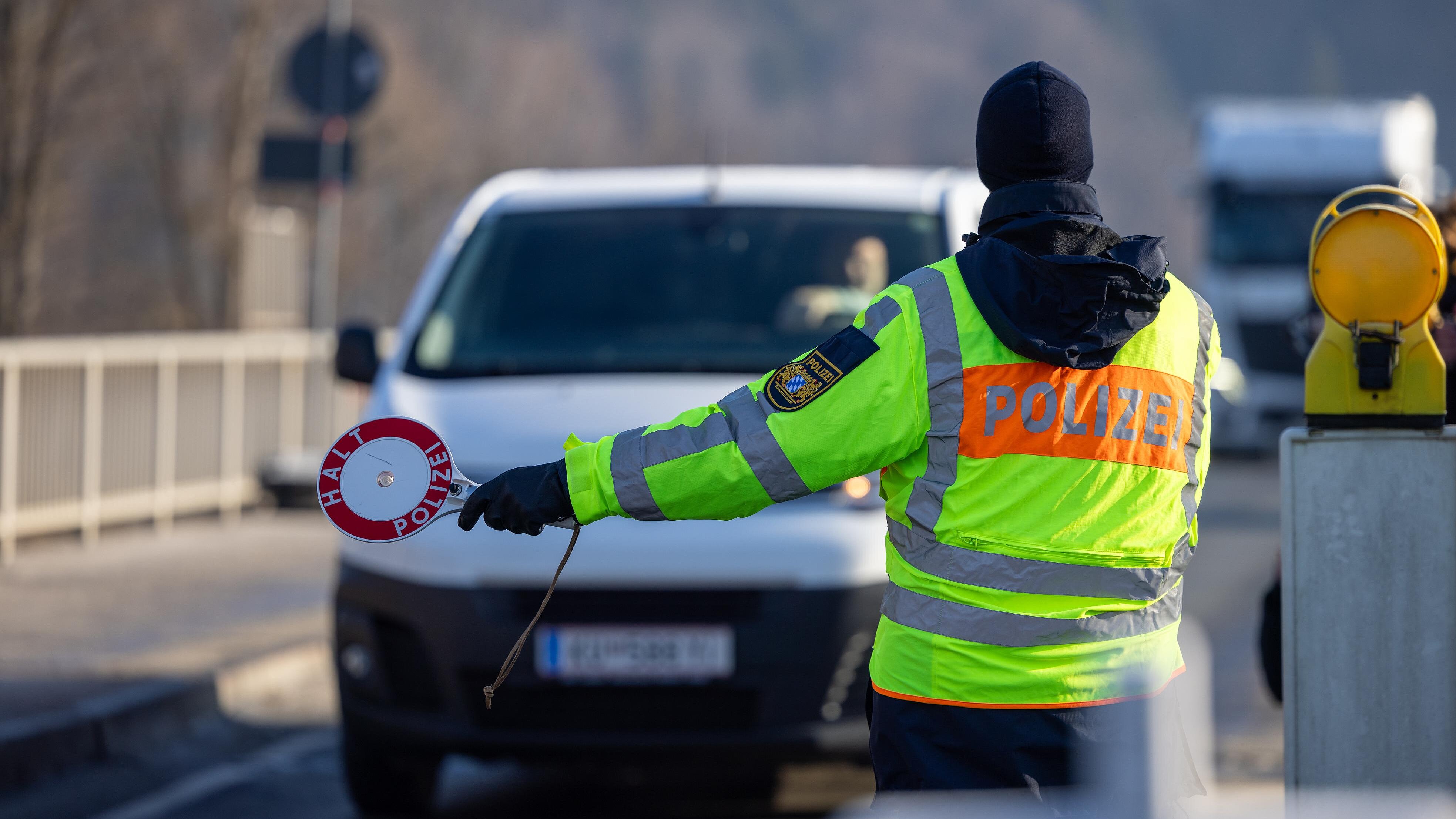 Polizist in Warnweste mit Polizeikelle stoppt einen weißen Van auf Straße