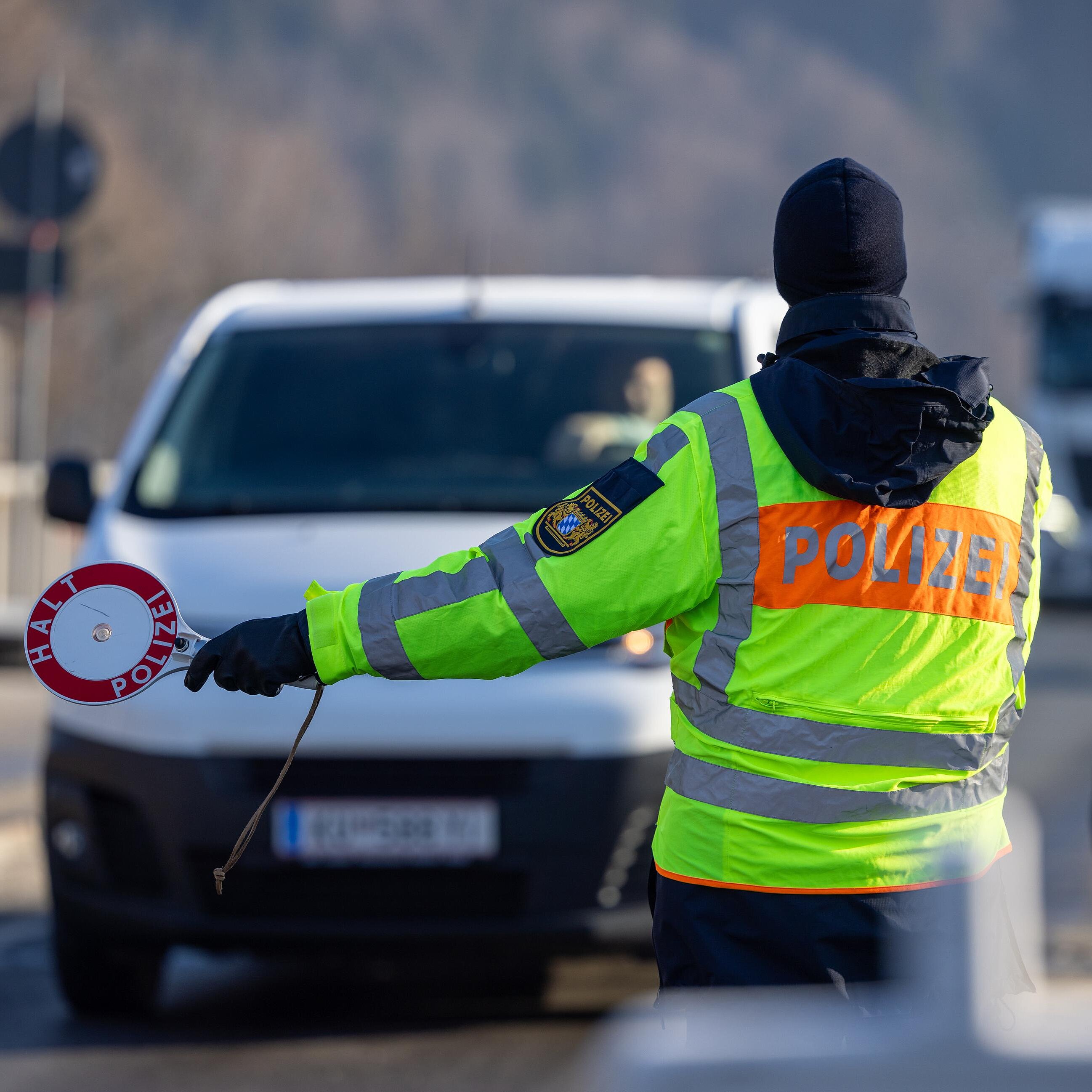 Polizist in Warnweste mit Polizeikelle stoppt einen weißen Van auf Straße