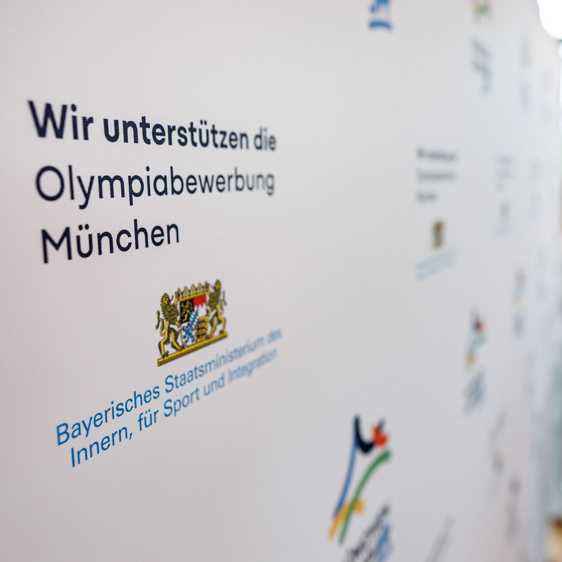Auf dem Bild ist eine Pressewand zu sehen, auf der die Unterstützung der Olympiabewerbung signalisiert wird sowie verschiedene Logos abgebildet sind
