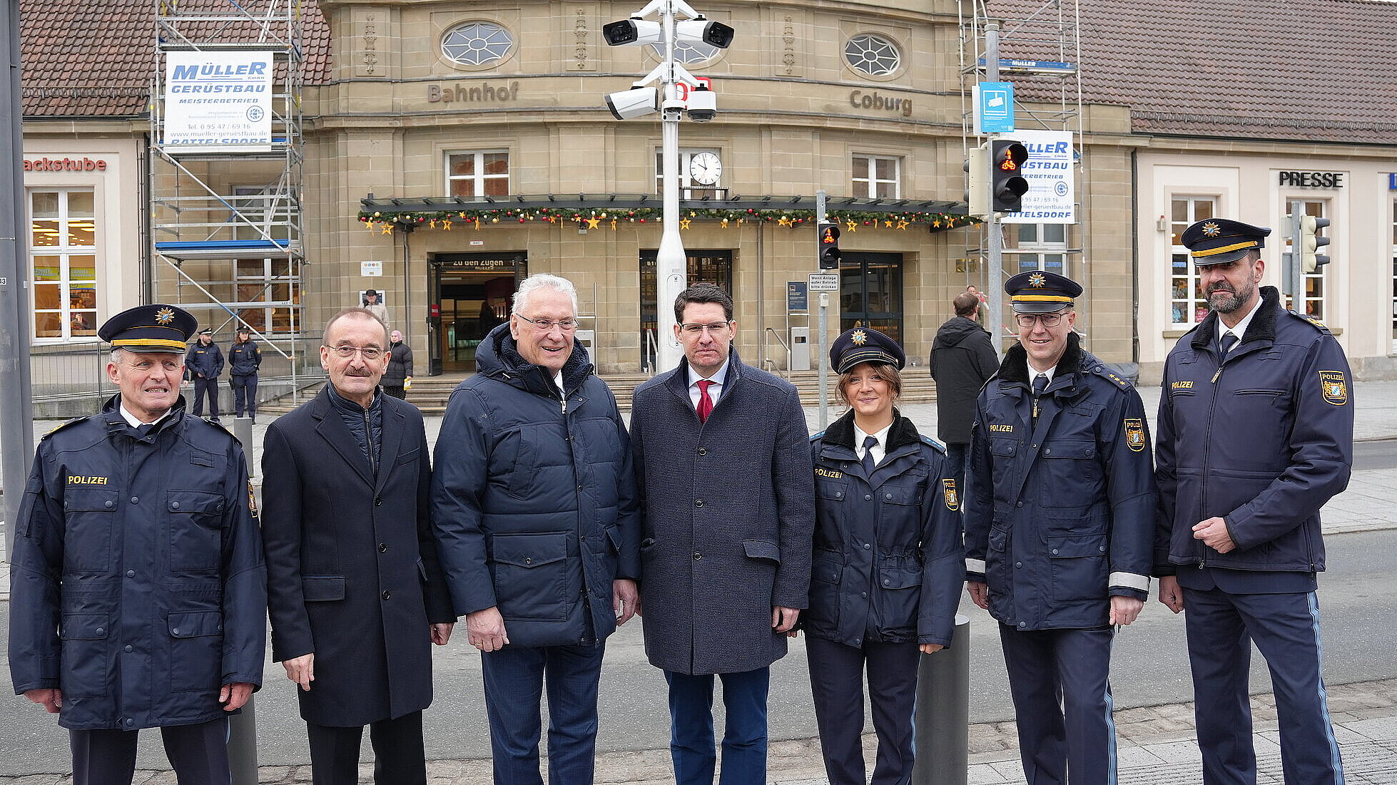 Auf dem Bild ist Innenminister Joachim Herrmann mit Offiziellen von Polizei und Stadt vor einem Überwachungsmasten am Coburger Bahnhof zu sehen.