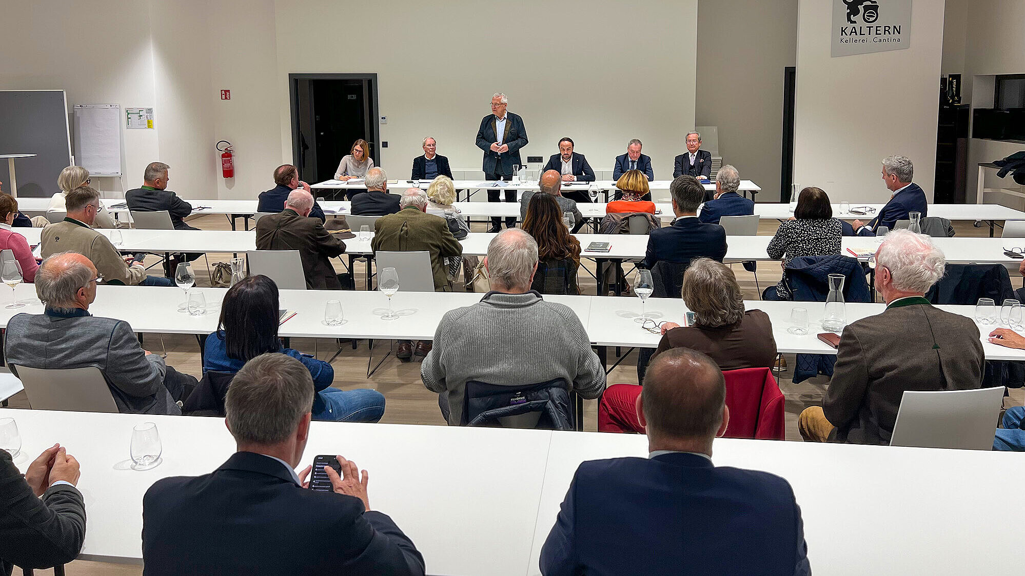 Versammlung in einem Raum, Innenminister Joachim Herrmann steht und hält eine Rede, Teilnehmer blicken zu Herrmann.