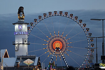Beleuchtetes Riesenrad und Löwenbräuturm vor Abendhimmel auf dem Oktoberfest