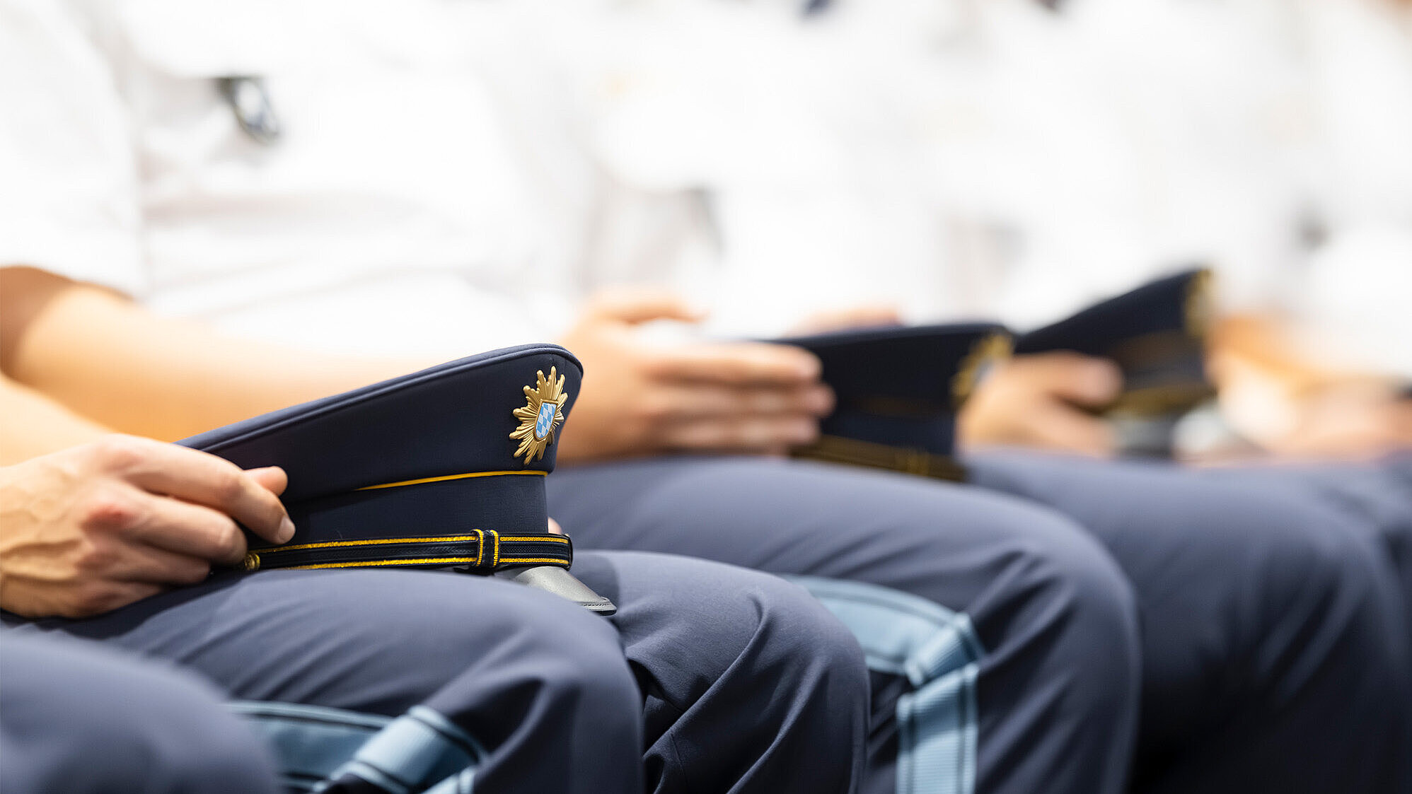 Detailaufnahme von Polizisten sitzend in der Reihe mit Hüten auf dem Schoß