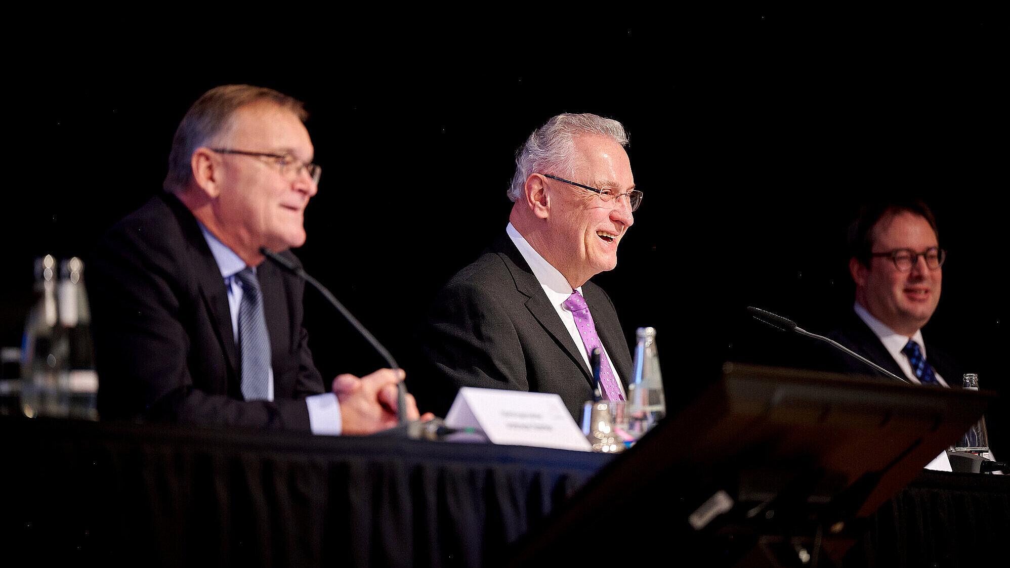 Innenminister Joachim Herrmann lachend auf dem Podium, neben ihm der Oberbürgermeister sowie der Regierungspräsident.