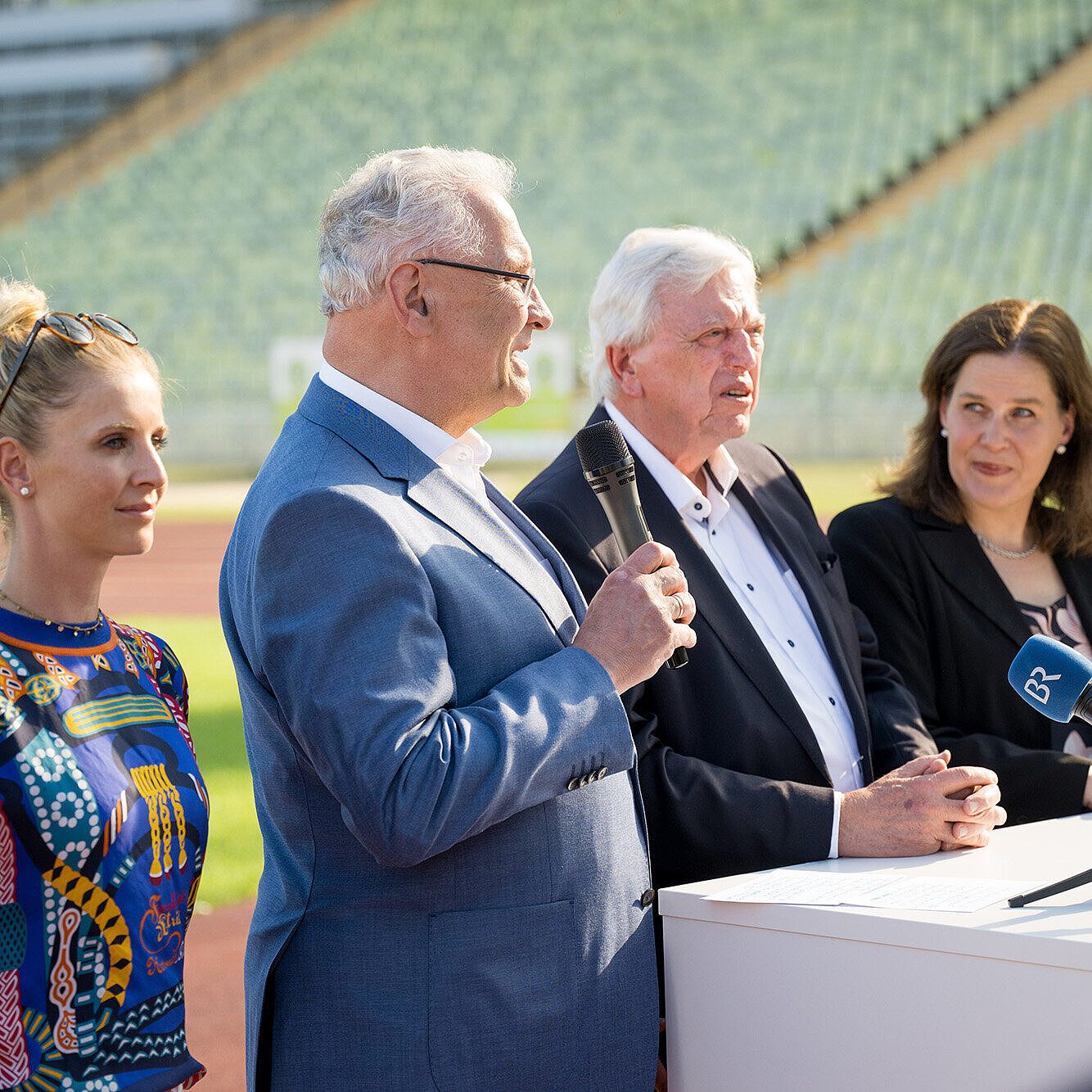 Gruppenbild von links Jessica von Bredow-Werndl Springreiterin, Innenminister Joachim Herrmann mit Mikrofon in der Hand, Bürgermeisterin Verena Dietl, Ministerpräsident Dr. Markus Söder stehen auf der Tartbahn im Olympiastadion vor einem weißen Tisch