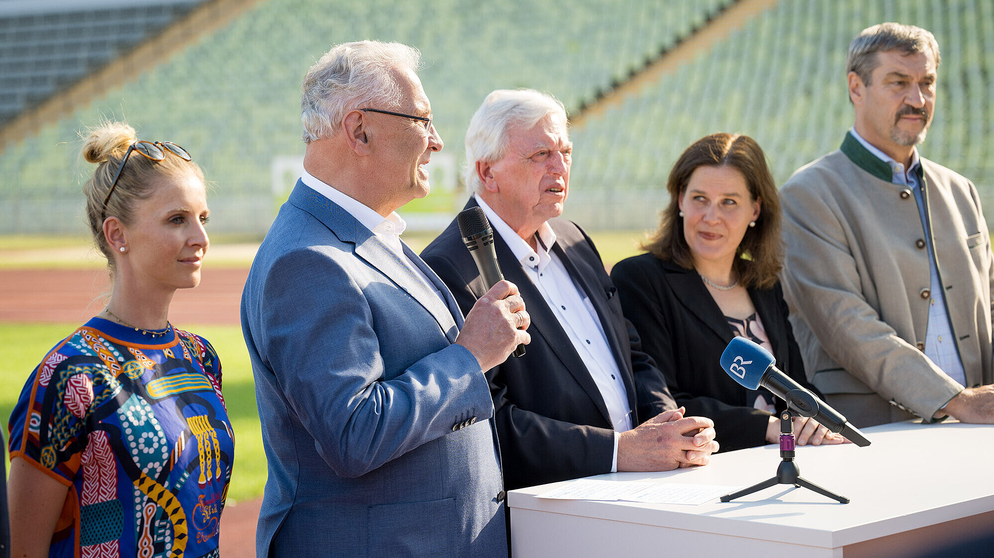 Gruppenbild von links Jessica von Bredow-Werndl Springreiterin, Innenminister Joachim Herrmann mit Mikrofon in der Hand, Bürgermeisterin Verena Dietl, Ministerpräsident Dr. Markus Söder stehen auf der Tartbahn im Olympiastadion vor einem weißen Tisch