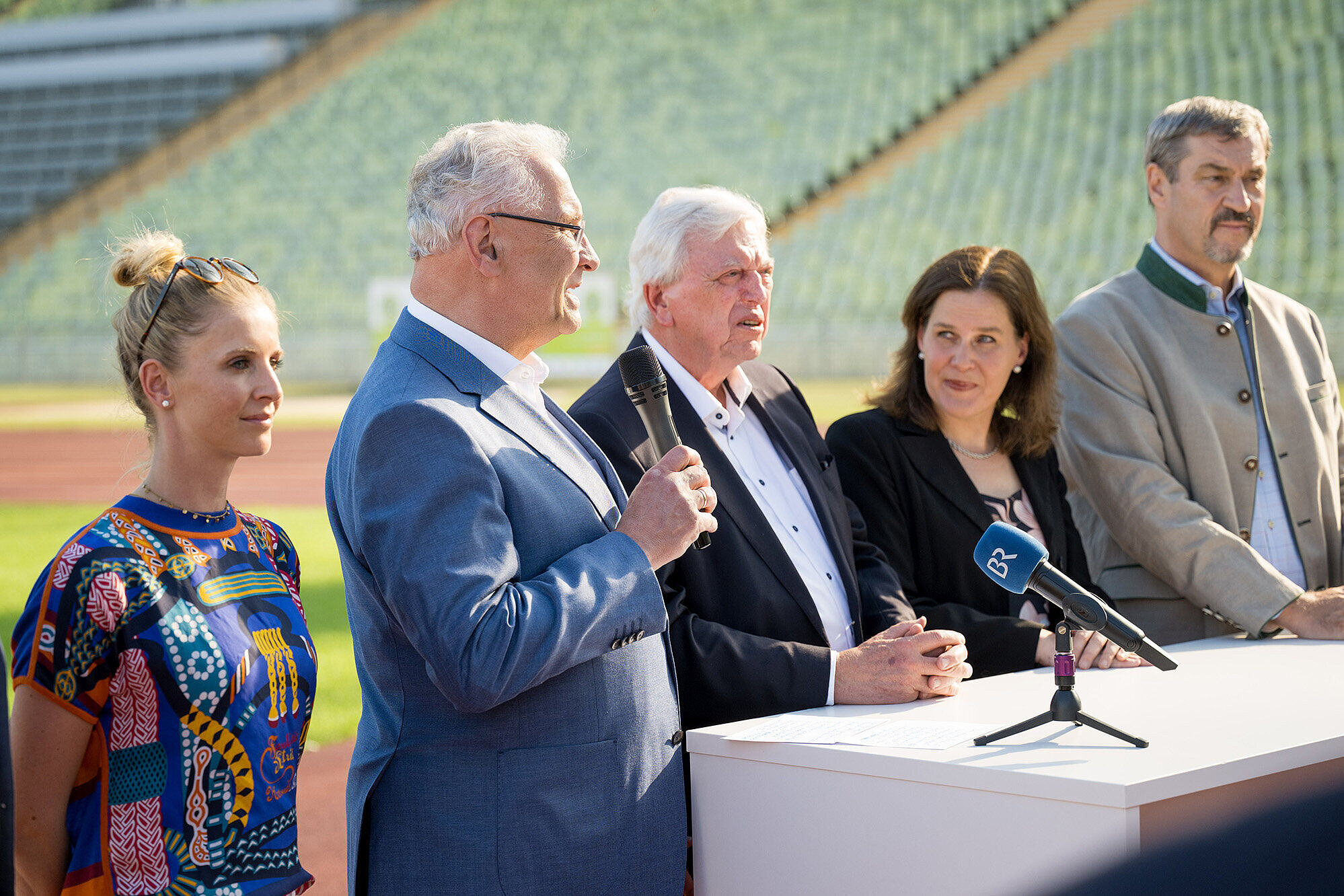 Gruppenbild von links Jessica von Bredow-Werndl Springreiterin, Innenminister Joachim Herrmann mit Mikrofon in der Hand, Bürgermeisterin Verena Dietl, Ministerpräsident Dr. Markus Söder stehen auf der Tartbahn im Olympiastadion vor einem weißen Tisch