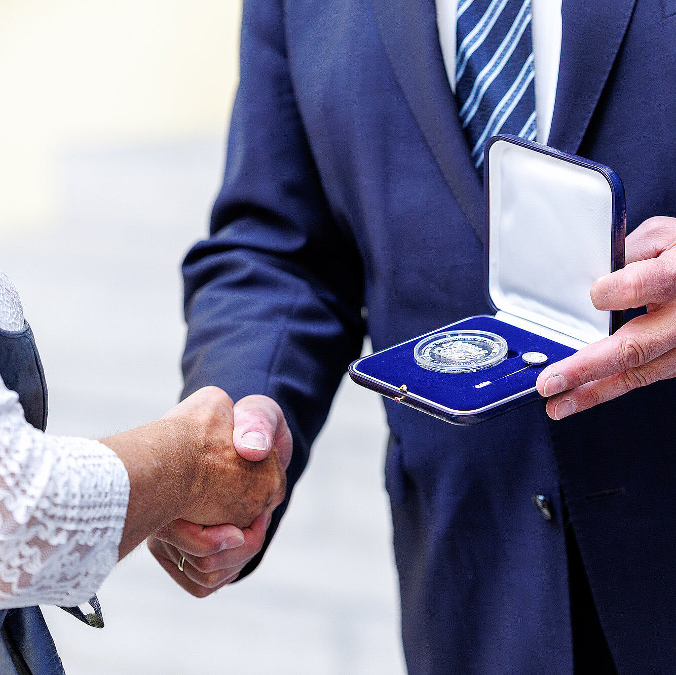 Detailaufnahme Händeschütteln und Aushändigung Medaille in Schachtel