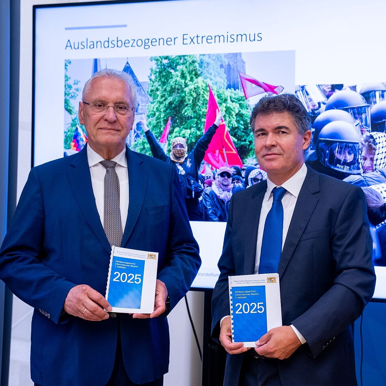 Auf dem Bild sind Innenminister Joachim Herrmann und LfV-Präsident Manfred Hauser zu sehen, wie diese die Verfassungsschutzinformationen für das 1. Halbjahr 2025 in die Kamera halten.