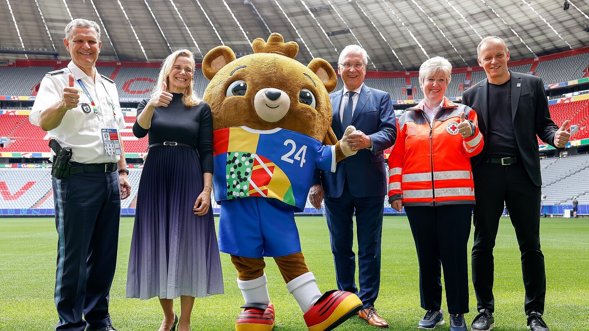 Gruppenfoto mit Vertretern der Sicherheitskräfte, Herrmann und Maskottchen auf Fußballfeld