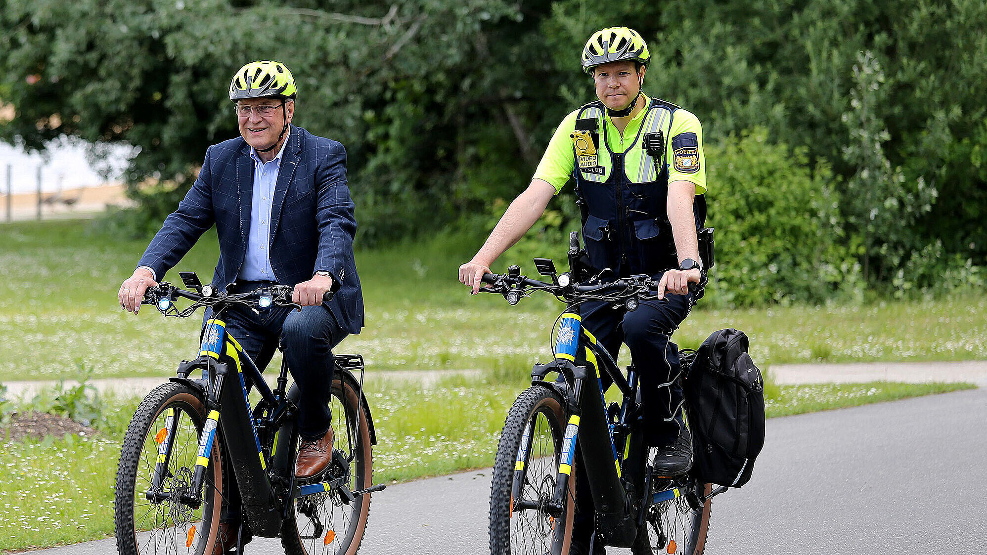 links Innenminister Joachim Herrmann und ein Polizist auf einem Fahrrad fahrend  mit Fahrradhelm auf Fahrradstraße