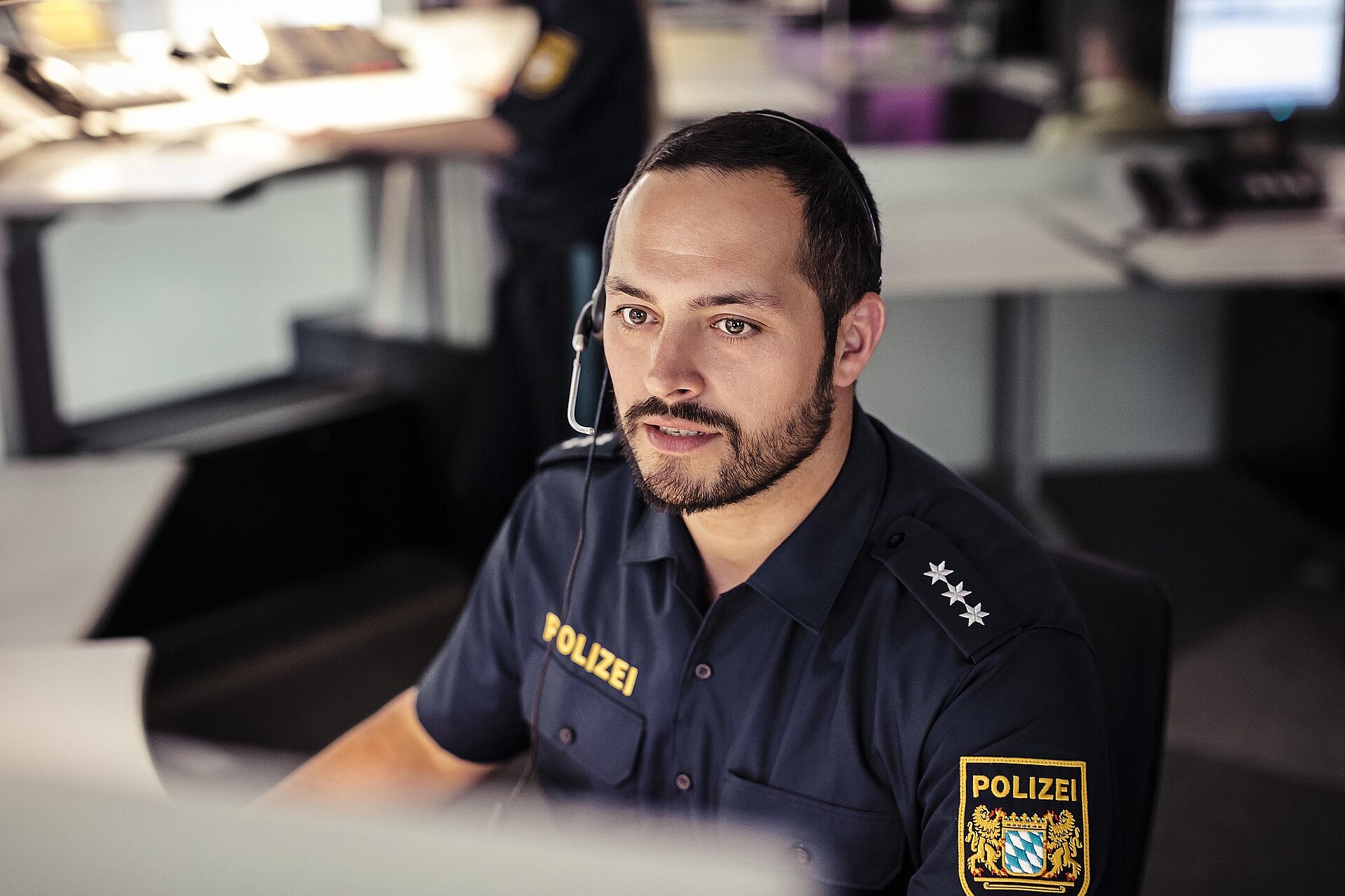 Polizist in kurzärmeliger Uniform mit Headset telefonierend am Computerarbeitsplatz