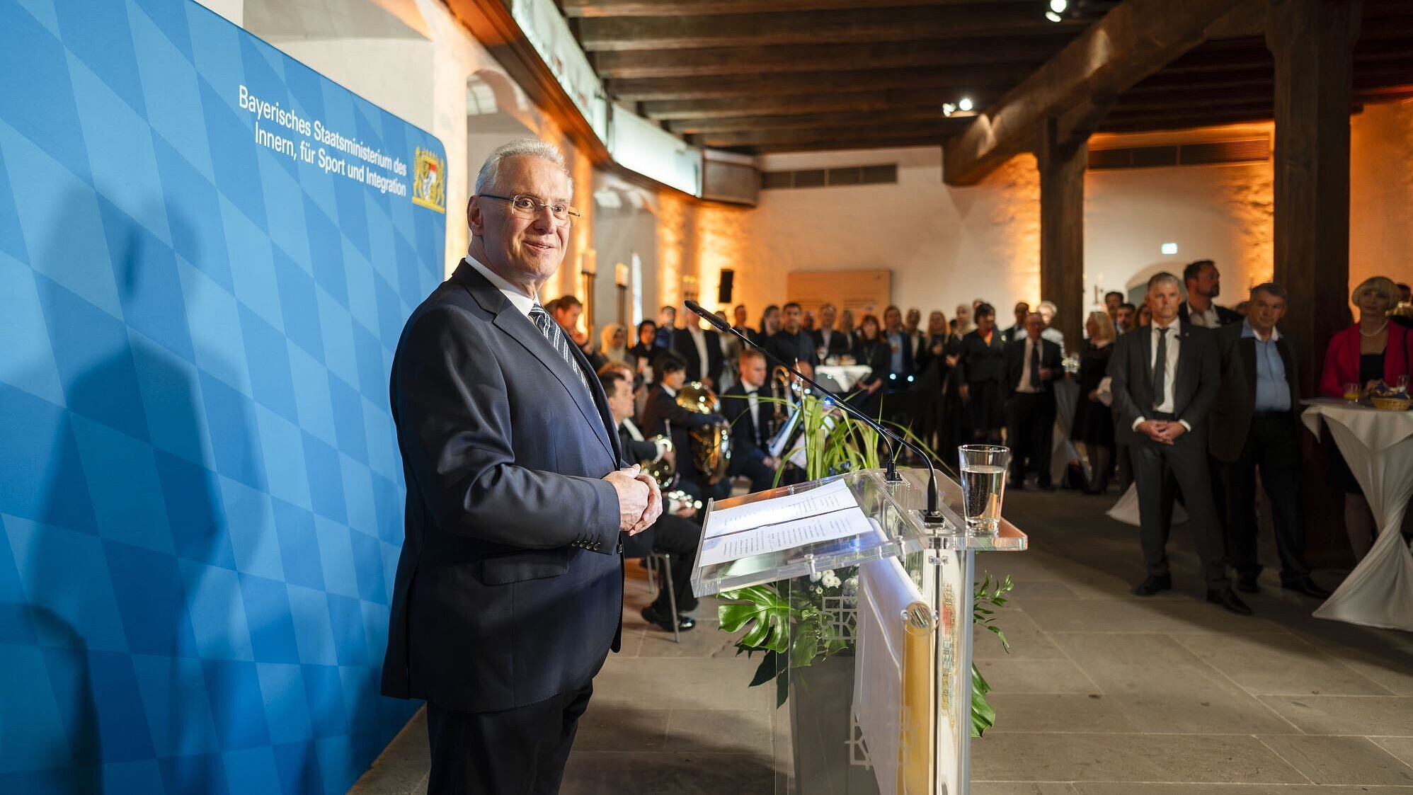 Auf dem Bild ist Innen- und Integrationsminister Joachim Herrmann bei seiner Rede an die Neubürgerinnen und Neubürger zu sehen und wie er diesen freundlich zulächelt.
