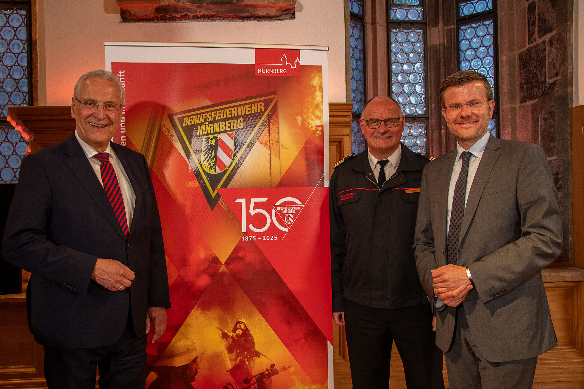 Innenminister Joachim Herrmann steht mit Oberbürgermeister Marcus König und Volker Skrok von der Feuerwehr Nürnberg neben einem Roll-up im historischen Rathaussaal