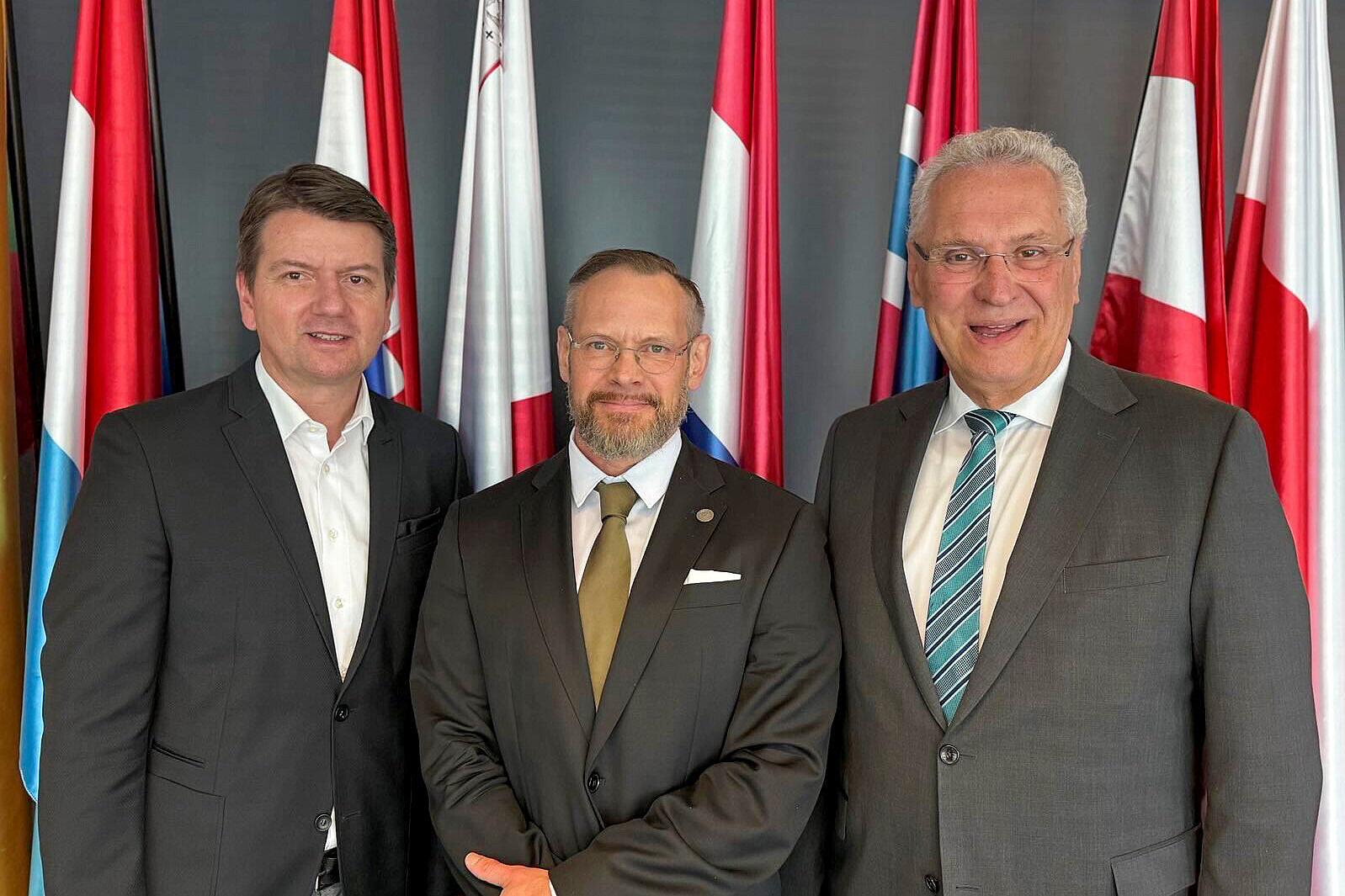 links Innenstaatssekretär Sandro Kirchner, rechts Innenminister Joachim Herrmann mit Blick in die Kamera vor einem Fahnenset
