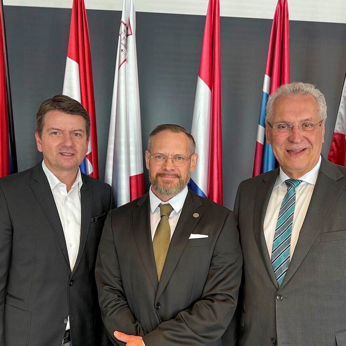 links Innenstaatssekretär Sandro Kirchner, rechts Innenminister Joachim Herrmann mit Blick in die Kamera vor einem Fahnenset
