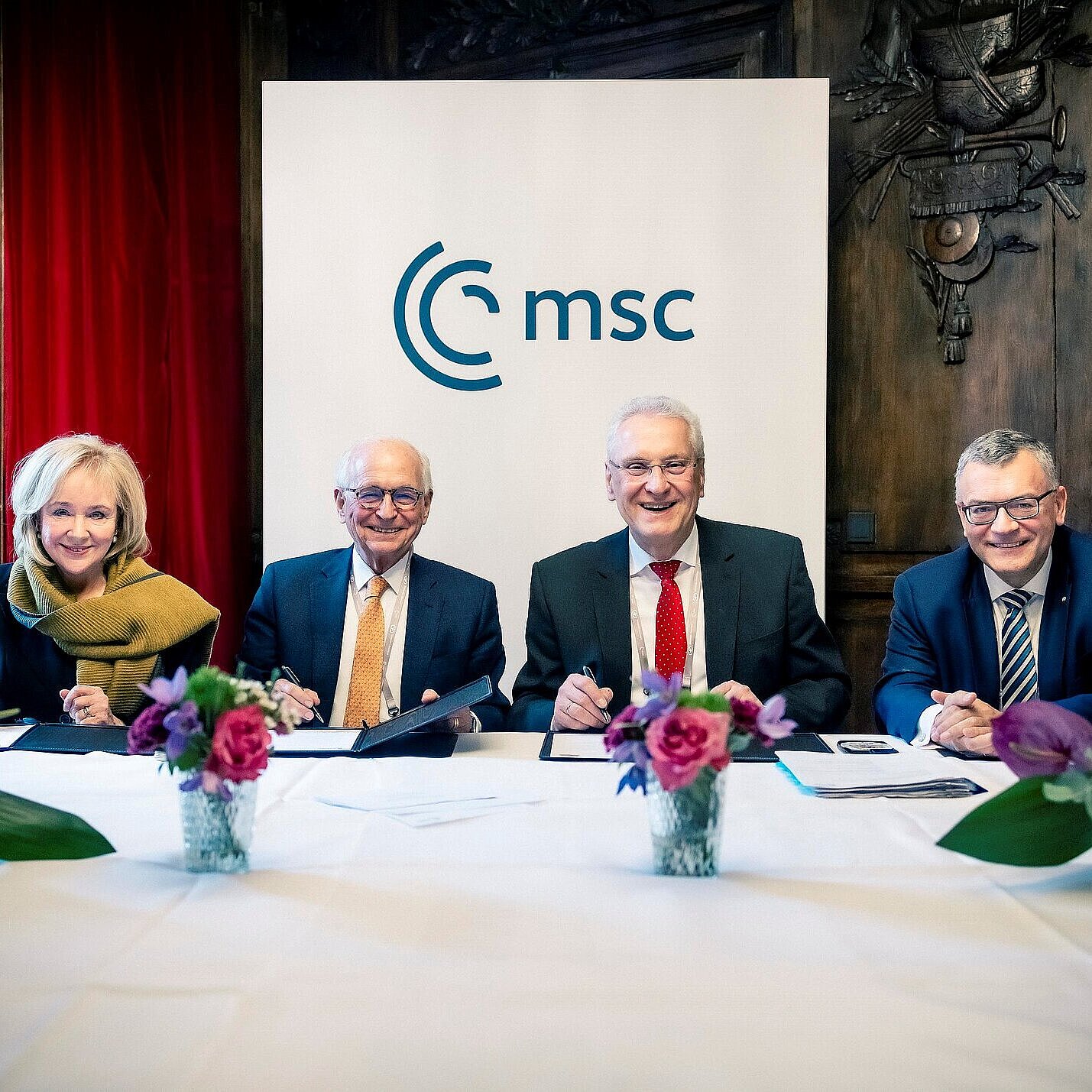 Vier Personen sitzen an einem Tisch, hinter ihnen ein Banner mit der Aufschrift "MSC".