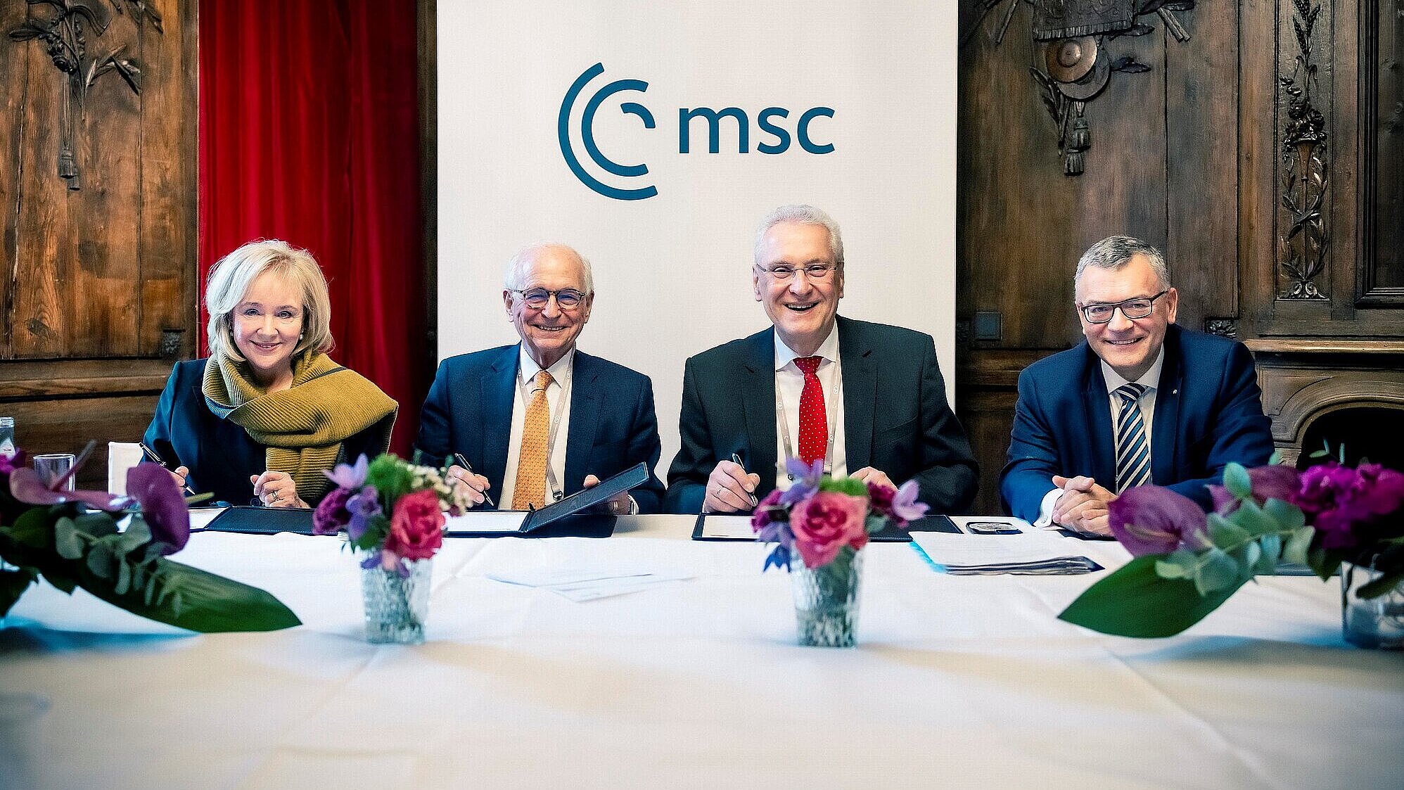 Vier Personen sitzen an einem Tisch, hinter ihnen ein Banner mit der Aufschrift "MSC".