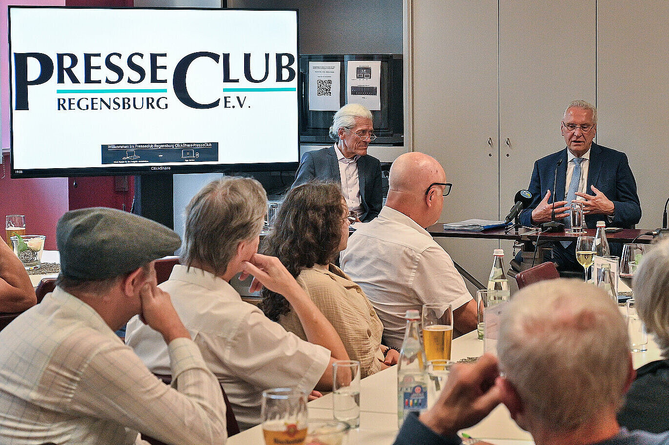 Innenminister Herrmann in Diskussion mit Blickkontakt zum Publikum, im Hintergrund der Schriftzug PresseClub auf einem Bildschirm.