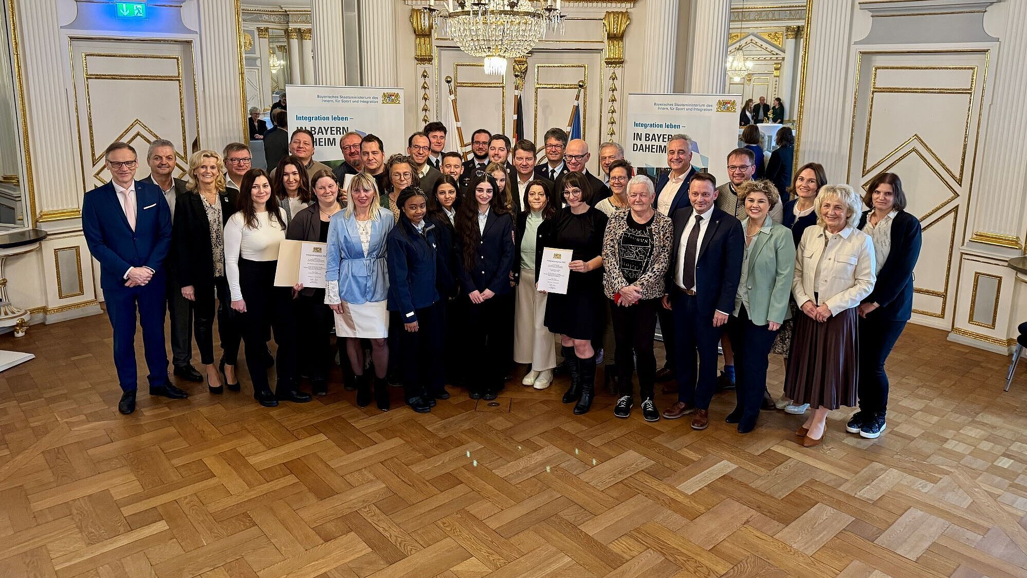 Eine Gruppe von geehrten Personen mit Honorationen in einem schönen Festsaal.