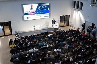 Blick von oben auf Publikum, Herrmann am Rednerpult bei Präsentation