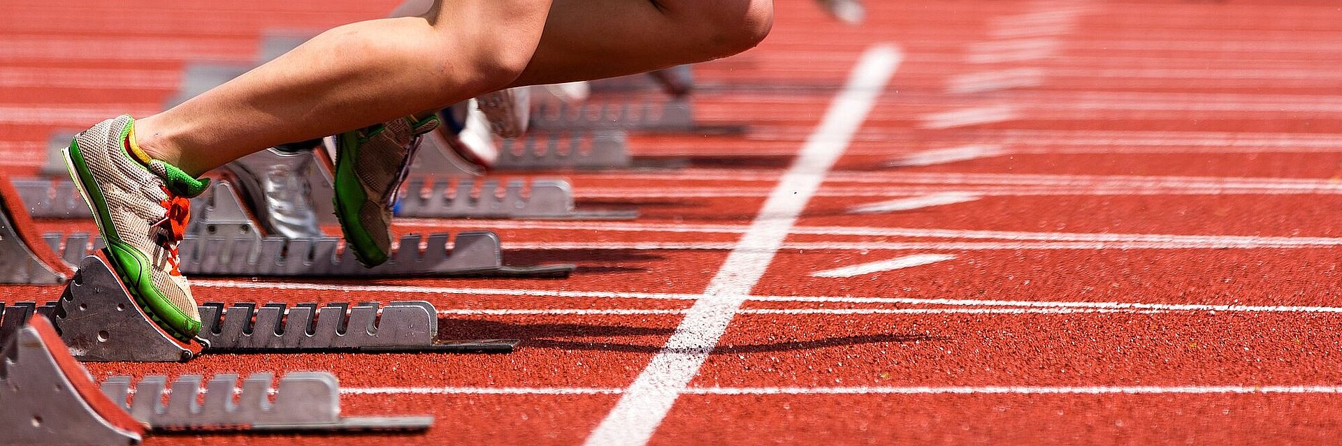 Tartbahn im Stadion mit Starter im Startblock - man sieht nur die Beine