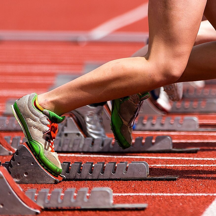 Tartbahn im Stadion mit Starter im Startblock - man sieht nur die Beine