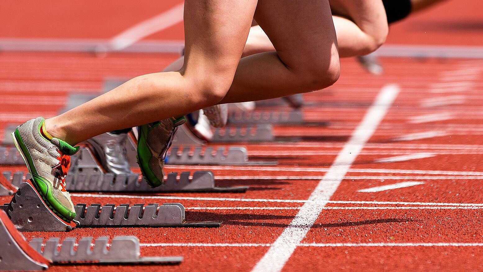 Tartbahn im Stadion mit Starter im Startblock - man sieht nur die Beine