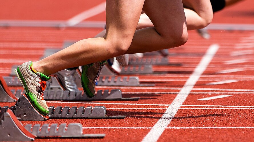 Tartbahn im Stadion mit Starter im Startblock - man sieht nur die Beine