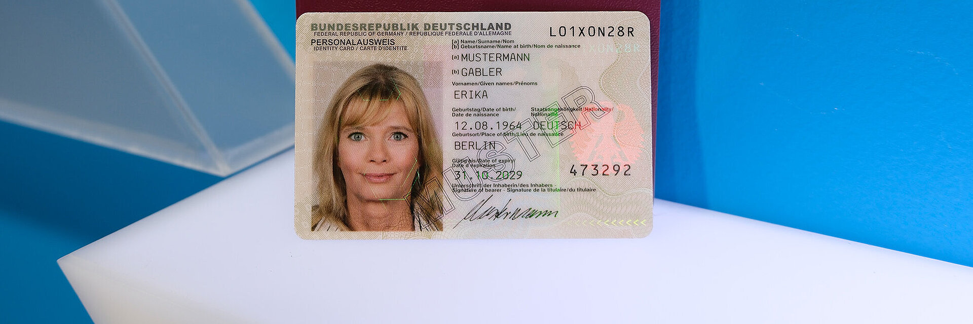 Ein Muster des Personalausweises mit sichtbarem Hologramm steht vor rotem Reisepass der Bundesrepublik Deutschland mit goldenem Adler