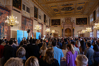 Innenminister Joachim Herrmann am Rednerpult bei seiner Rede in der Münchner Residenz zum Neubürgerempfang Publikum schaut zur Bühne